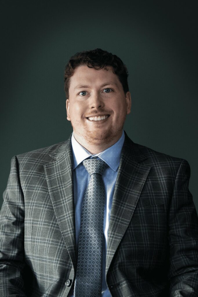 A smiling man in a plaid suit with a blue shirt and tie, appearing friendly.