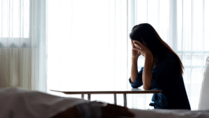 A person with hands on head, sitting on a desk, near a window with sheer curtains, symbolizing emotional distress related to non pecuniary damages Alberta 2025 compensation.