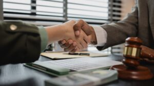 Hands shaking over a desk with legal documents and a gavel, symbolizing a legal settlement agreement.