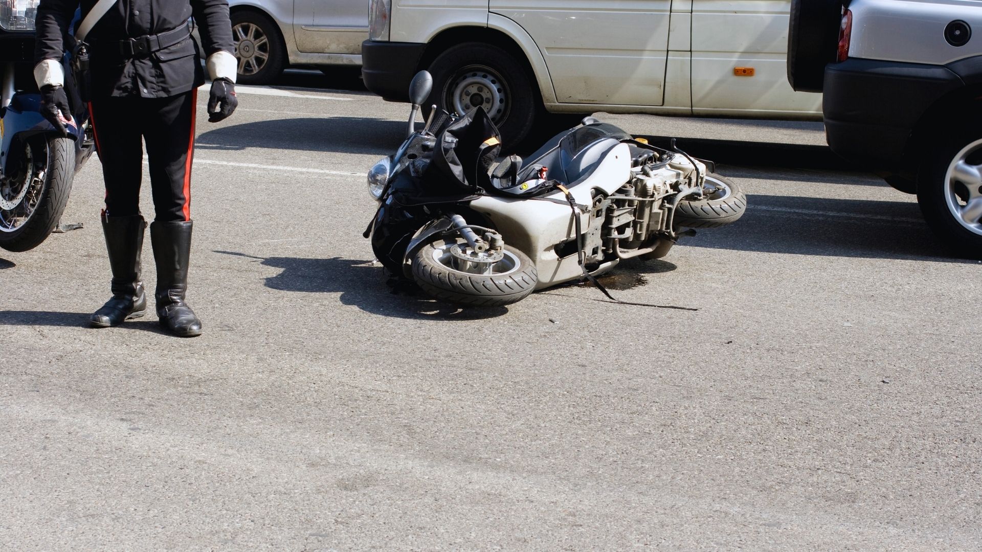 A police officer standing near a crashed motorcycle on a road, with another bike and vehicles in the background, at 11:27 PM CEST on September 16, 2025.