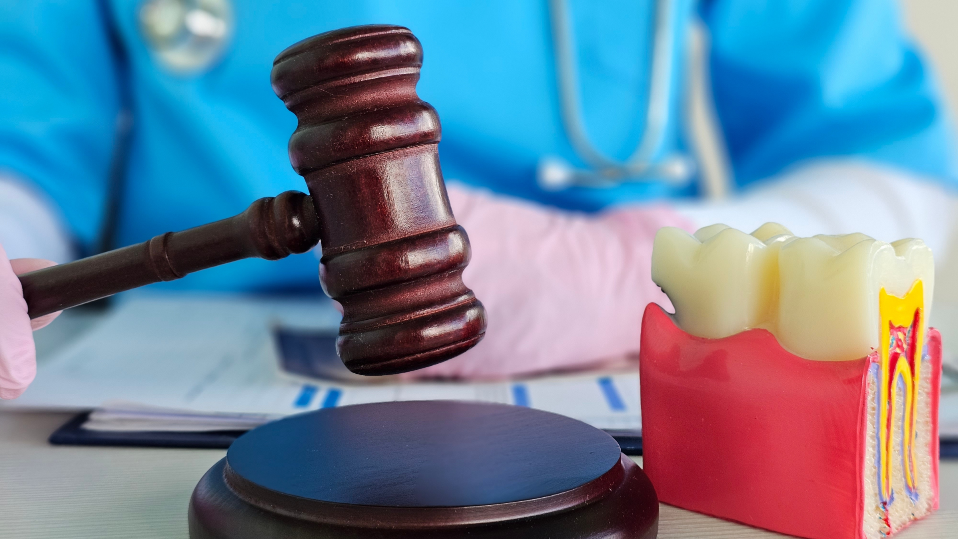 A gavel being held by a person in blue medical scrubs, with a stethoscope and a model of teeth on the table, symbolizing a legal or medical decision related to dentistry.