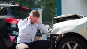 Injured man holding neck between two crashed vehicles, representing the question should I accept first settlement offer car accident victims face.