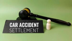 Gavel with wooden figure and car accident settlement nameplate on green background, illustrating 50/50 shared fault settlements and what shared blame means for claims