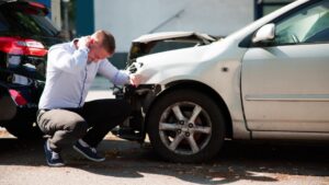 Man experiencing neck pain after car collision with damaged white vehicle showing whiplash injury for Alberta settlement cap 2026 guide