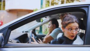 Startled driver leaning out of car window after a parking lot accident, raising the question of who is at fault under Alberta law.