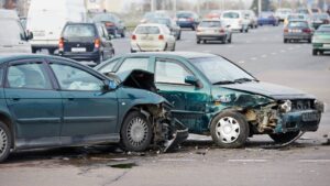 Both Drivers at Fault Car Accident Alberta What It Means for Your Claim. Two green cars severely damaged in a front-to-side collision on a busy multi-lane road, debris scattered across the pavement with traffic visible in the background.